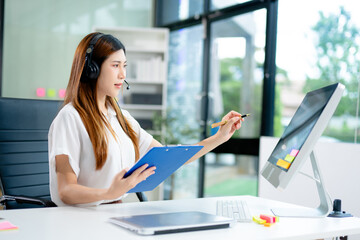 Young woman in headset taking notes during customer support session. Great for themes like online...