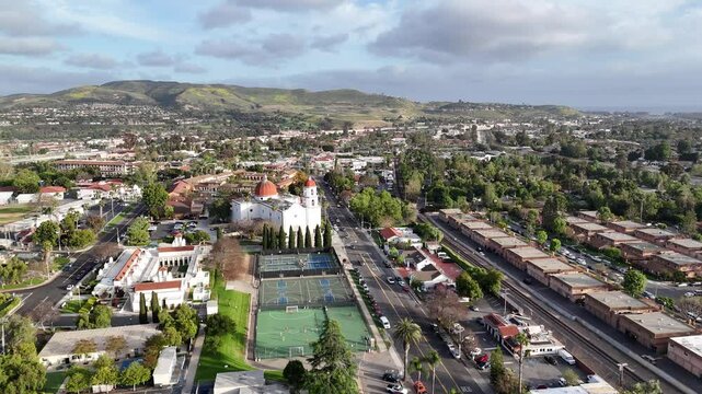 Aerial view over San Juan Capistrano, California, featuring the historic mission, library, sports courts, and an Amtrak train pulling into the downtown station.