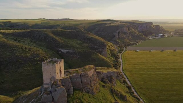 Drone shot of the medieval Oreja Castle perched on a hilltop at golden hour near Aranjuez, Spain. Scenic sunset over rural fields and rocky landscape.