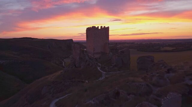 Drone shot of the medieval Oreja Castle perched on a hilltop at golden hour near Aranjuez, Spain. Scenic sunset over rural fields and rocky landscape.