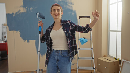 Woman painting living room in apartment with roller wearing casual clothes and smiling celebrating...