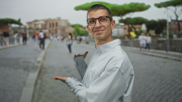 Fototapeta Man in glasses gestures at famous italian street with people, showcasing vibrant urban life on a sunny day in rome's historic cobblestone setting.