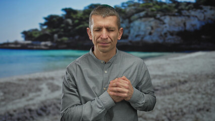 Man with clasped hands stands contemplatively on a scenic beach, ocean waves gently meeting the...