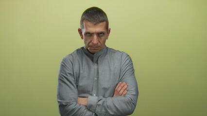 Man in gray shirt crossing arms against yellow wall isolated confidently, displaying serious expression and intense gaze, suggesting thoughtfulness and determination.