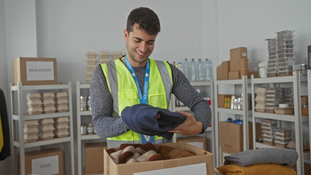 Man picks up shirt and starts folding it inside warehouse bins for donation while wearing top hispanic volunteer donation worker vest.