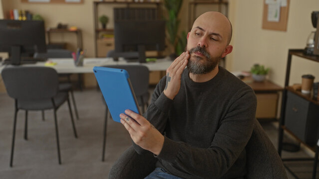 Bald man using tablet in cozy office with modern decor and workspace essentials around, showcasing professional and focused atmosphere. - Powered by Adobe