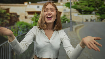 Young blonde woman in white crop top bare arms beckons on cobblestone street; urgency plea frustration.