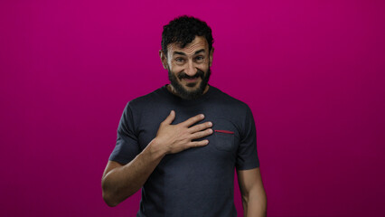 Hispanic man with beard expressing surprise and gratitude against vibrant pink background, hand on...