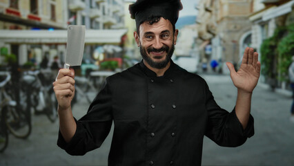 Hispanic man chef in black uniform with beard holds cleaver smiling on a bustling street background...