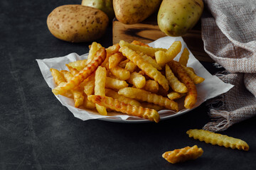 Freshly Cooked Crinkle Cut Fries on a Plate with Raw Potatoes in Background