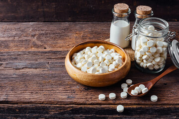 White Tablets in Wooden Bowl and Glass Jar on Rustic Wooden Table