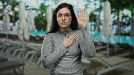 Woman making oath gesture by swimming pool setting with a serious expression, conveying sincerity...