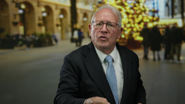 Senior man in business suit animatedly conversing on a bustling outdoor street against festive urban backdrop.