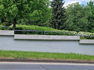 Massive concrete retaining wall by the road with tubular railing. Flowering bushes in the...