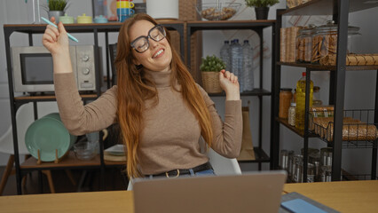 Woman smiling indoors with long red hair in office setting featuring desk and shelves, suggesting a...