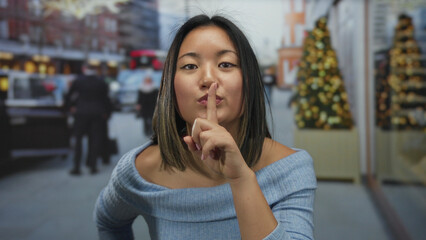 Woman gesturing silence on a city street adorned with festive decorations, embodying tranquility...