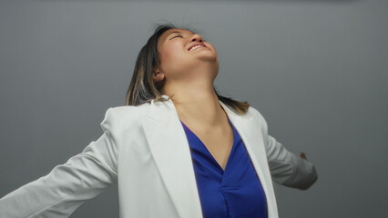 Young chinese woman rejoices with arms outstretched against isolated grey background wearing white...