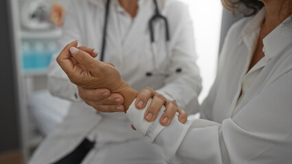 Woman doctor examining wrist of patient in clinic, highlighting healthcare interaction in a...
