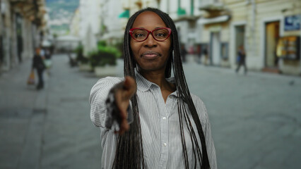 Woman extends hand for handshake on urban street with blurred city background suggesting friendly...