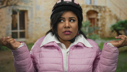Woman in pink jacket and helmet outdoors in city setting represents plus size latina expression on...