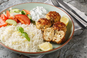 Delicious chicken meatballs stuffed with feta cheese served with lemon rice, tzatziki sauce and vegetable salad close-up in a plate on the table. horizontal