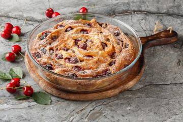 Fresh cherry filo pie with vanilla custard cream and powdered sugar close-up in glass bowl on wooden board. horizontal