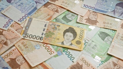 South korean banknotes featuring various denominations and historical figures are scattered across a surface, representing the won currency in vibrant and detailed designs.
