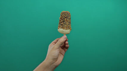 Hand holding icecream with chocolate isolated against green background, depicting a simple treat...