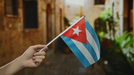 Caucasian man holding cuban flag on city street captures national pride in colorful urban setting.