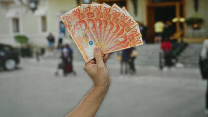 Man holding multiple 20-peso philippine banknotes outdoors in a city street setting.