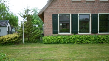 Blurred view of a charming house exterior with brick walls and green shutters surrounded by lush shrubbery, creating a serene suburban setting with a defocused background.