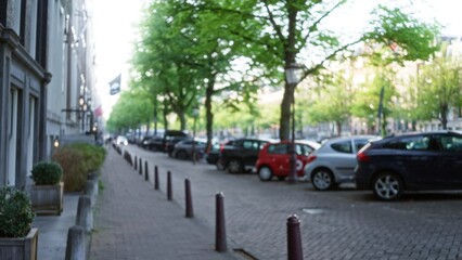 Blurred view of a european city street lined with parked cars, trees, and buildings showcasing a peaceful urban scene.