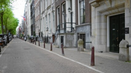 Blurred street view in amsterdam shows traditional dutch architecture and lush green trees with a focus on the serene atmosphere and timeless european cityscape.