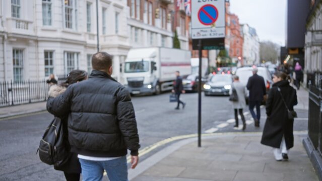 Urban street scene with blurred people walking in winter clothing on a busy london road featuring man and woman amidst bokeh cars and historic buildings.