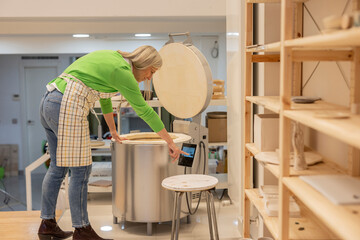 Ceramist woman setting temperature of kiln in workshop