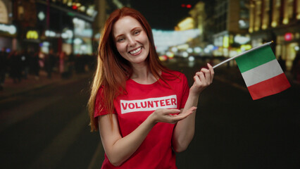 Woman with red hair smiling and holding italian flag, standing on a city street at night,...