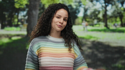 Fototapeta premium Woman smiling in colorful sweater enjoying park with trees in the background on a sunny day outdoors.