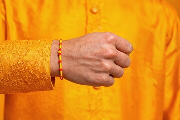 A man's hand with a yellow rakhi on his wrist. Traditional festive attire in golden yellow tones.