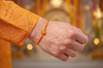 A man's hand with a yellow rakhi on his wrist. Traditional festive attire in golden yellow tones.