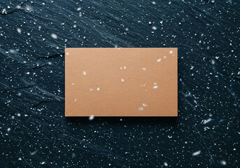 Blank kraft paper card mockup on dark wooden surface with falling snow