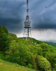 Tall radio tower stands prominently on hilltop amidst vibrant green woods in rainy mid-spring weather