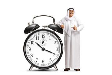 Middle eastern man in traditional clothes leaning on a big alarm clock and pointing