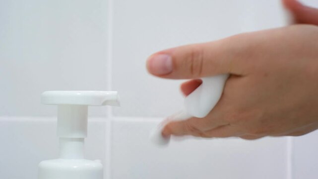 Female hands squeeze liquid soap with foam from white bottle.