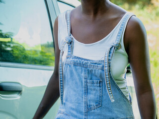 Young black female farmer wearing dungarees, white tank top, opening pickup truck door, preparing for agricultural work in rural landscape