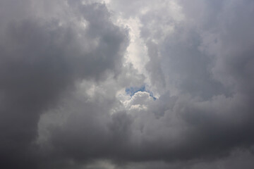 Dramatic Dark Grey Storm Clouds Gathering In The Sky, With A Small Patch Of Blue Sky And White...