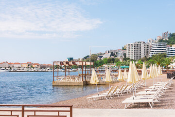 Obraz premium Empty sun loungers and closed umbrellas on the Adriatic coast. Summer beach infrastructure and seaside tourism in Budva, Montenegro