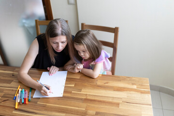 Mother helping daughter with homework, homeschooling on kitchen table