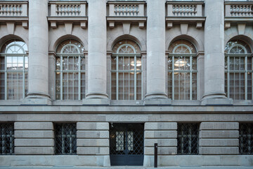 A detailed view of a classical stone building facade featuring large arched windows on the upper level, framed by imposing columns.