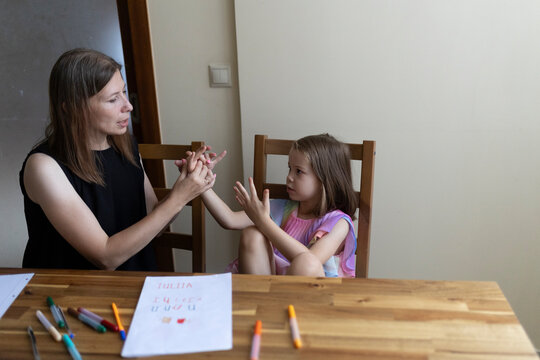 Teacher helping young girl learning sign language at home - Powered by Adobe