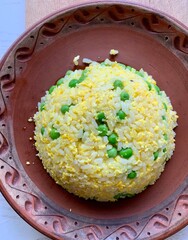 A vibrant dish of yellow rice mixed with green peas is beautifully presented in a traditional bowl...